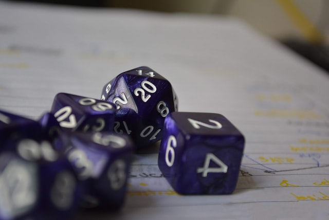 Purple polyhedral dice with white numbers rest upon a piece of lined paper with handwritten notes.